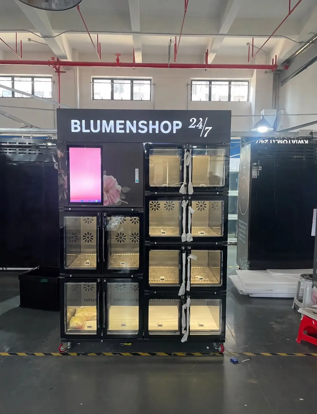 Aufgestellter Zwölffach-Automat in Schwarz, die Leuchtblende trägt die Beschriftung des Kunden.