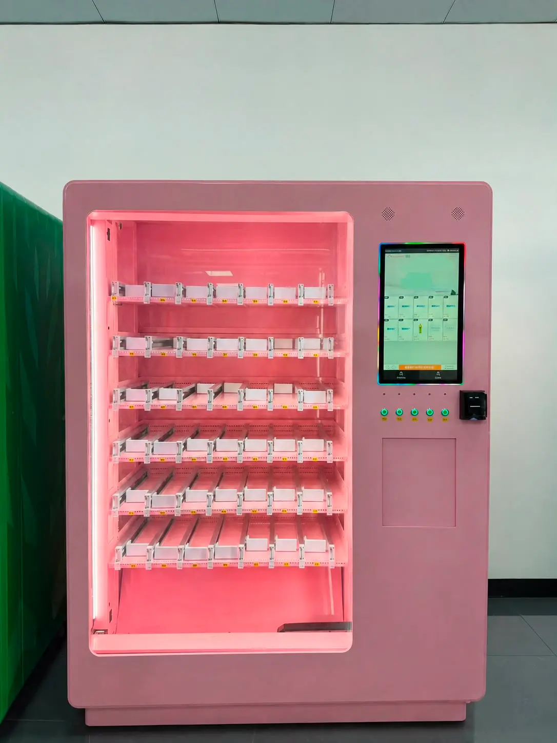 Ein Automat desselben Modells, ganzes Gerät: rosa Gehäuse, Gleitkanäle in mehreren Ebenen hinter beleuchtetem Glas, daneben Touchscreen und Kartenleser. Die Bahnen sind noch leer.